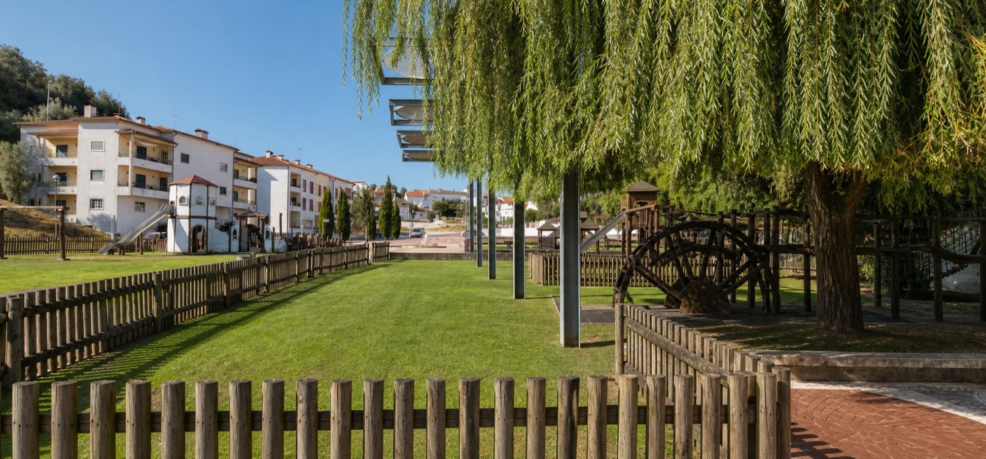 Shaded play area beneath willow trees in Parque das Águas Romanas