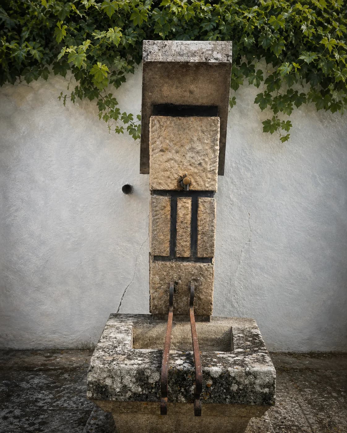 Stone public fountain beneath grapevine leaves in Penela